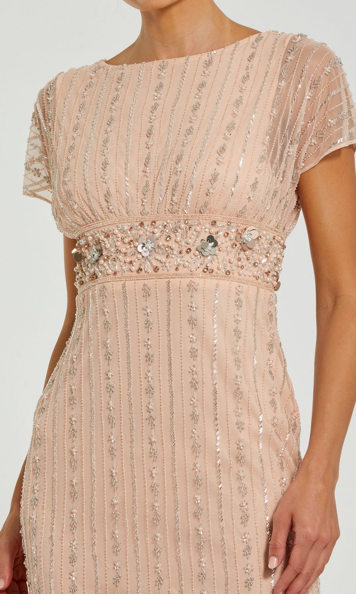 A woman wearing the Mac Duggal 94147 long formal dress, featuring short sleeves, blush pink fabric adorned with beaded pearl embellishments and vertical sequin detailing, and a decorated waistband.